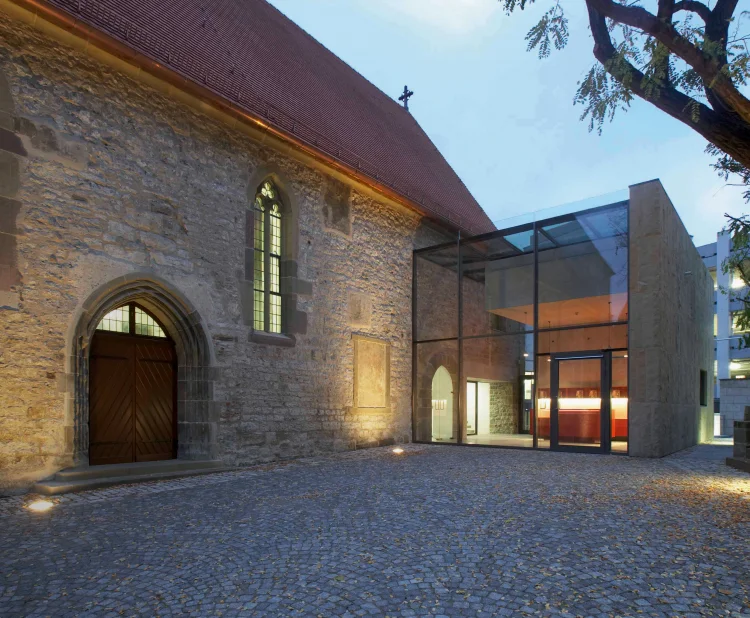 Außenansicht der Johanniterkirche Schwäbisch Hall mit modernem Glasanbau, Abenddämmerung